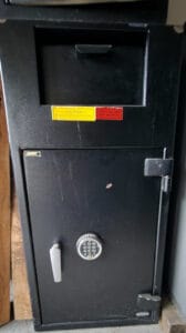 Black tall safe with a keypad dial and a white lever; yellow caution and red deposit stickers visible on the front door.