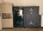 Row of safes in a garage: beige Fort Knox-style safe, dark green Remington safe, and a tall Browning safe beside a white chest-freezer on the right.