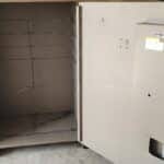20260806_170410 – The Safe Pros Open beige metal safe with an empty interior, showing brown steel shelves and welded seams, placed on a wooden pallet on a concrete floor.